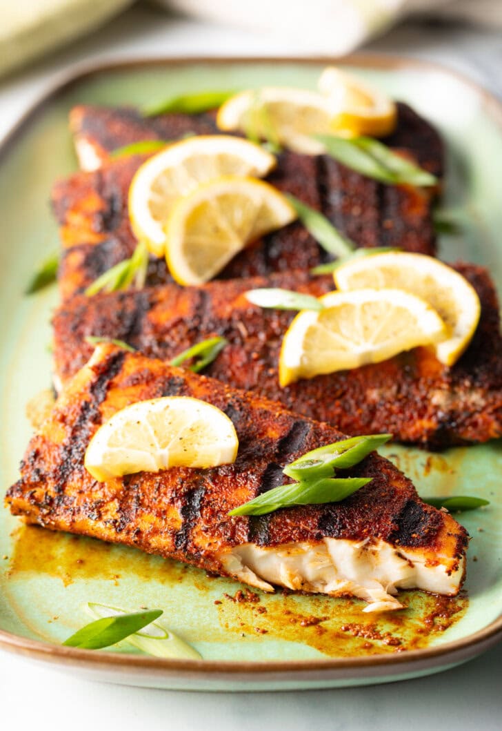 4 fillets of grilled mahi mahi topped with a slice of lemon and green onions. A bite has been removed from the fish to show the white flaky inside of the meat.