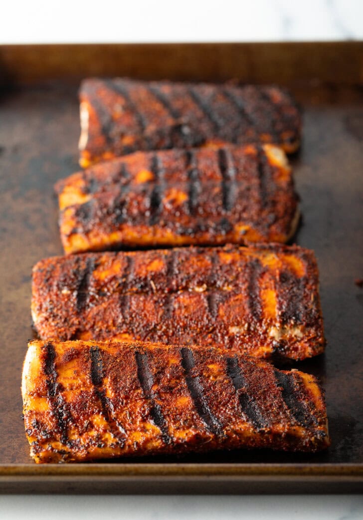 4 large fillets of grilled fish on a baking sheet coated with blackening seasoning.