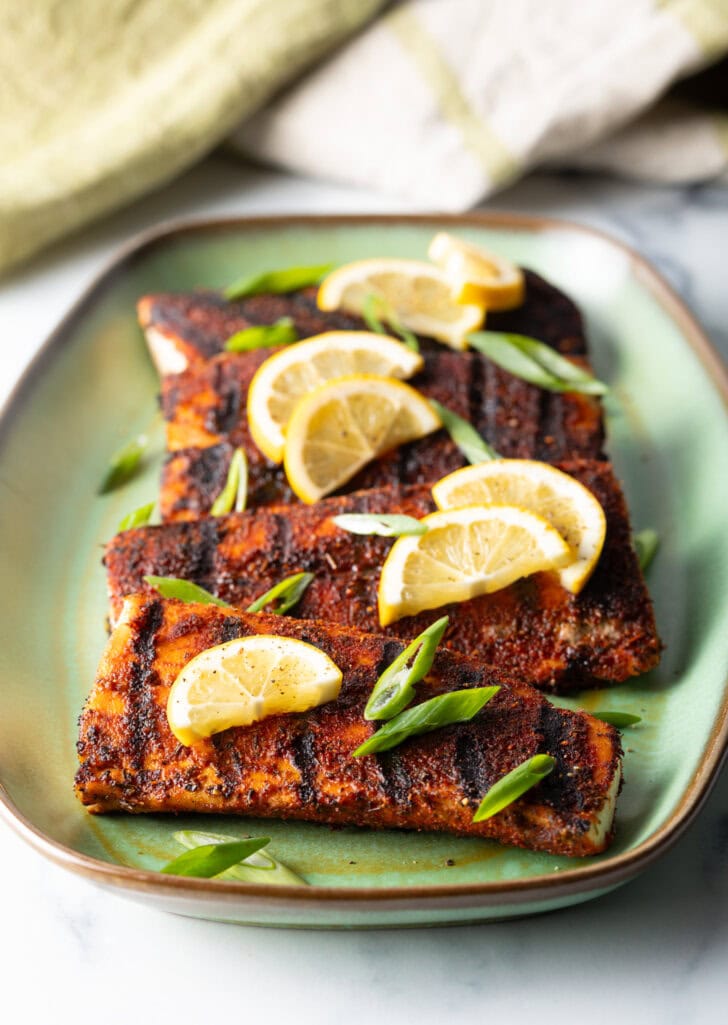 4 pieces of blackened and grilled fish, all topped with slices of lemon and green onions.