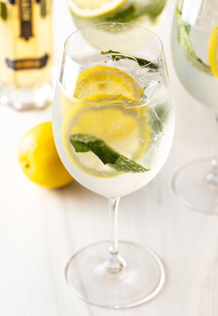 Finished hugo spritz recipe: 3 wine glasses each with clear alcohol, mint leaves, and lemon slices.