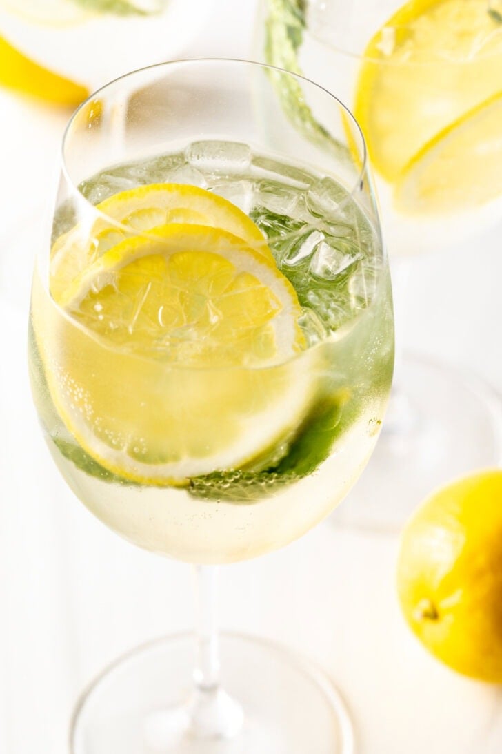 Wine glass with clear alcohol, mint leaves, and lemon slices.