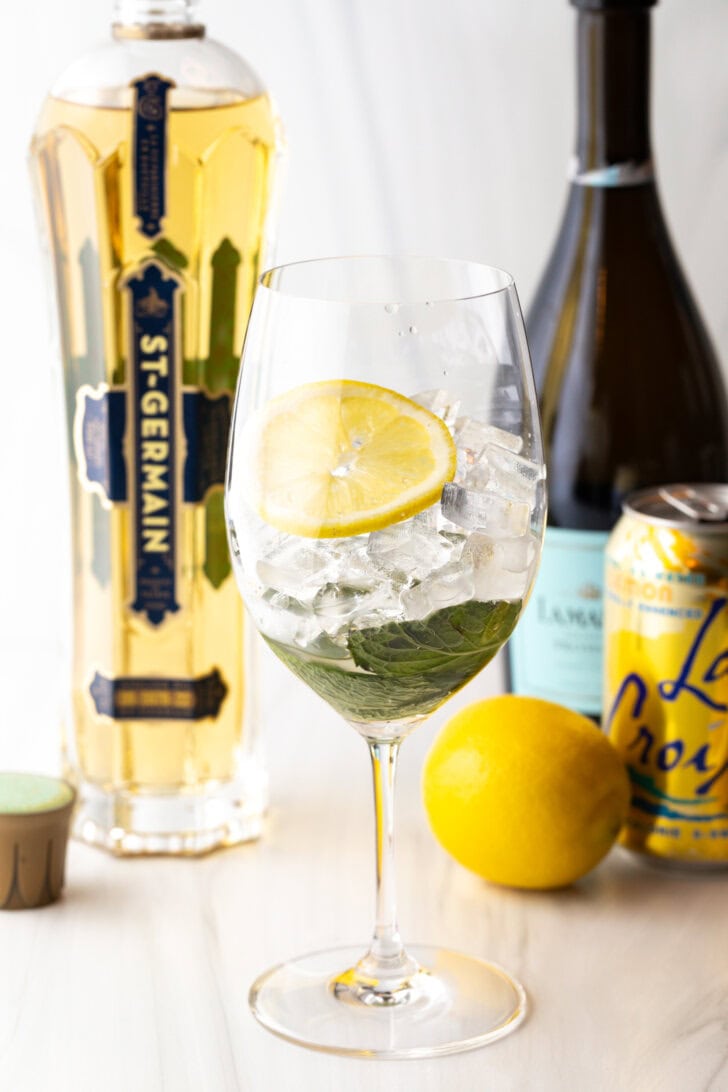 Wine glass filled with mint leaves, ice, and slice of lemon.