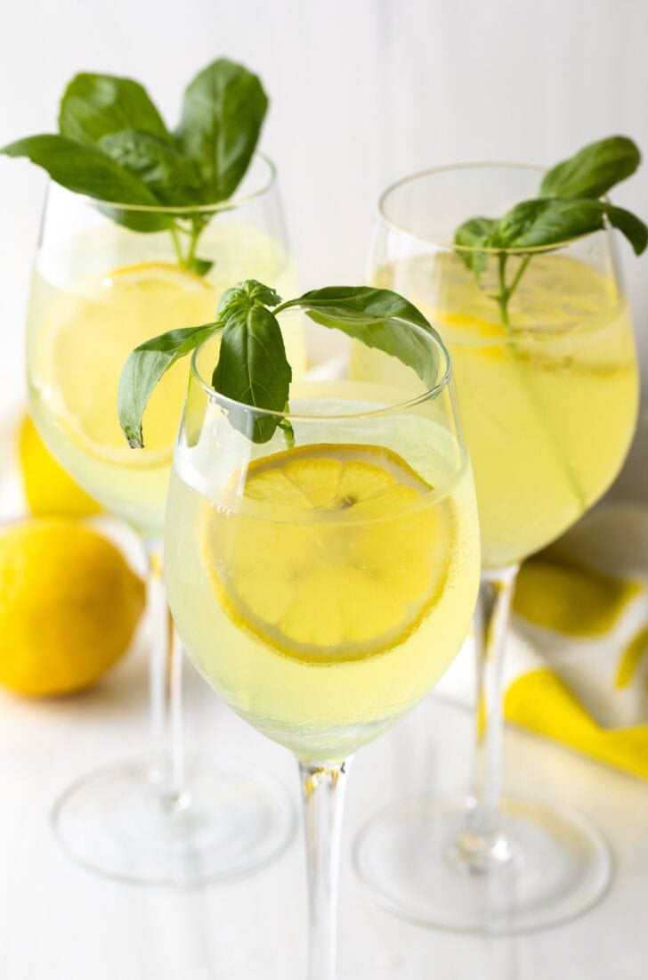 3 wine glasses each with limoncello spritz, fresh slices of lemon, and fresh mint leaves.