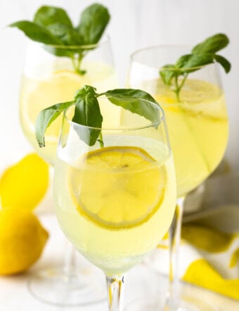 3 wine glasses each with limoncello spritz, fresh slices of lemon, and fresh mint leaves.