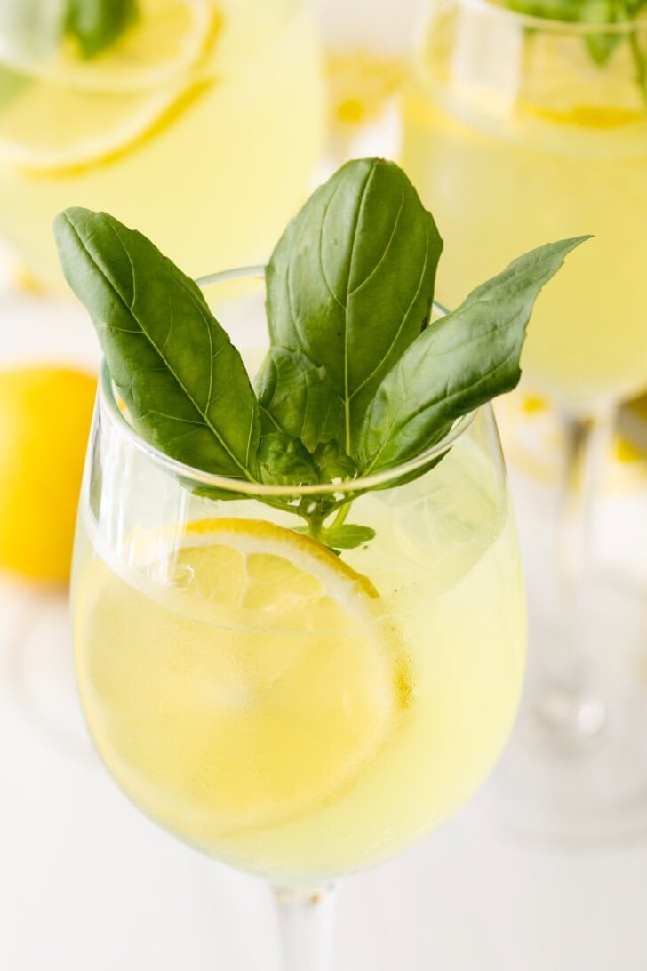 Wine glass with limoncello spritzer, fresh slices of lemon, and fresh mint leaves.