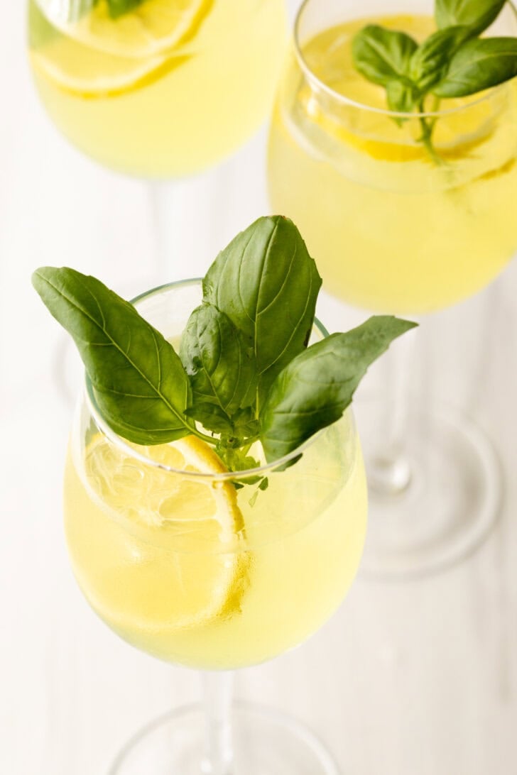 Wine glass with limoncello spritzer, fresh slices of lemon, and fresh mint leaves.
