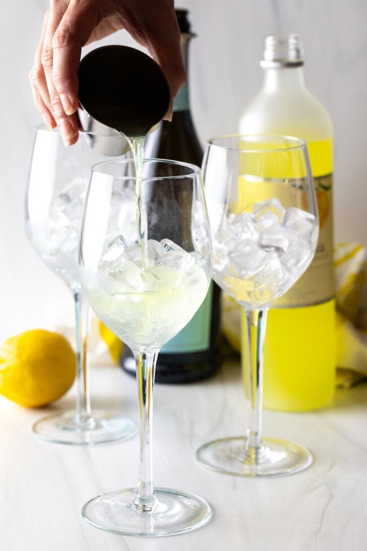 Hand adding limoncello into wine glasses half full of ice.