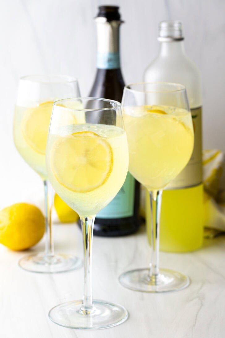 Garnishing 3 wine glass of spritzer with fresh lemon slices.