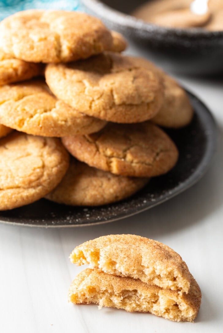 Plateful of Mexican cookies in the background. Two halves of broken cookie are stacked on top of each other closer to camera.