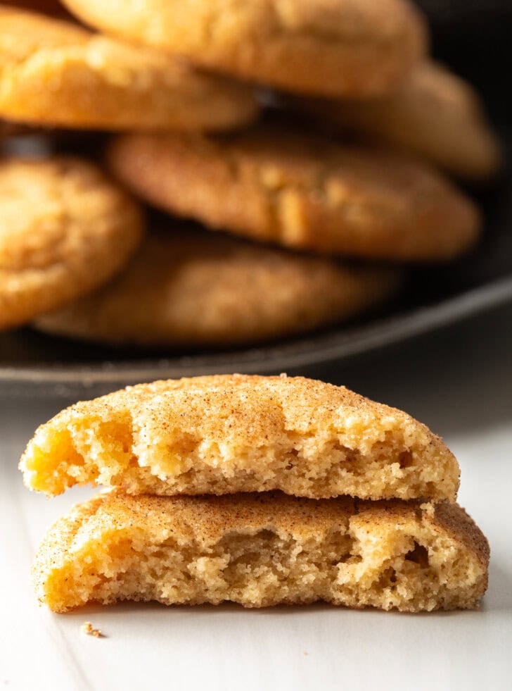 Plateful of Mexican cookies in the background. Two halves of broken cookie are stacked on top of each other closer to camera.