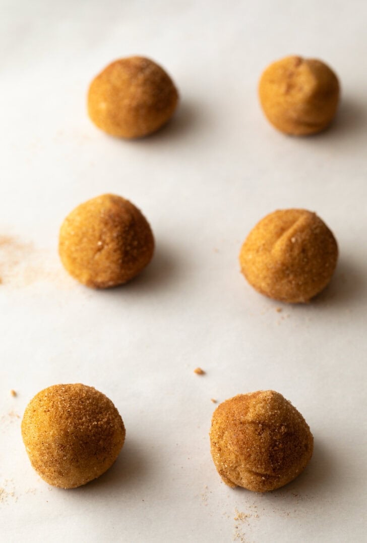6 cookie dough balls rolled in sugar, placed on a baking sheet.