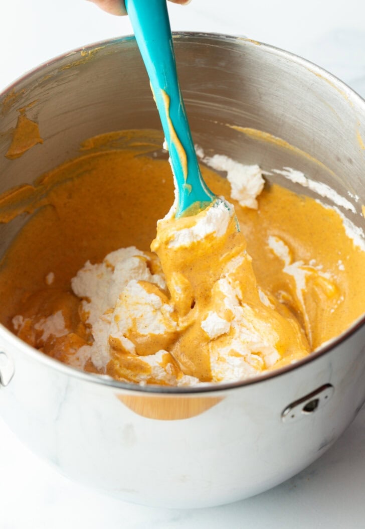 Pumpkin puree and cream cheese being mixed together with a blue spatula in a large metal bowl.