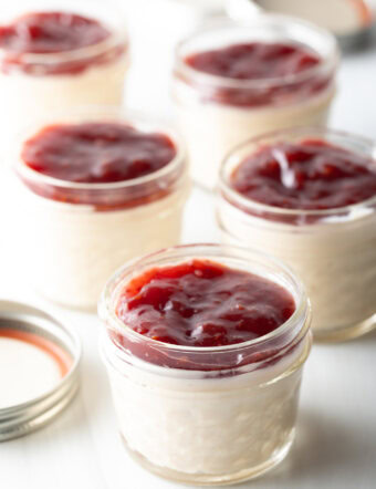 5 small glass jars of protein pudding topped with raspberry jam.