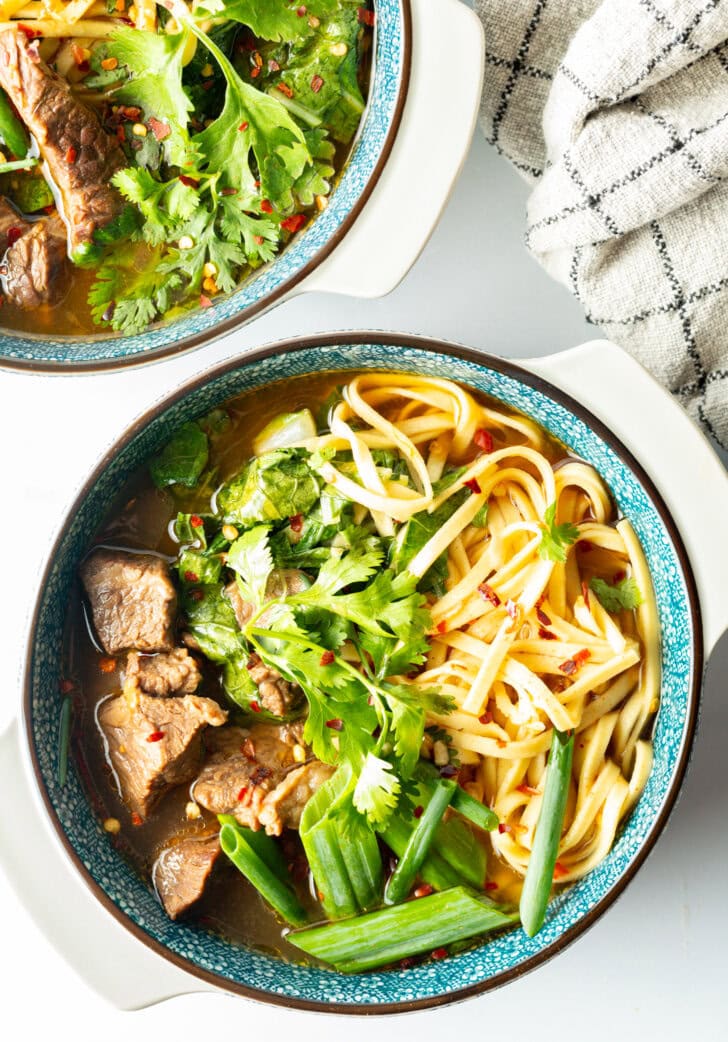 Top down view bowl of Taiwanese beef soup with noodles, green scallions, and chopped bok choy.