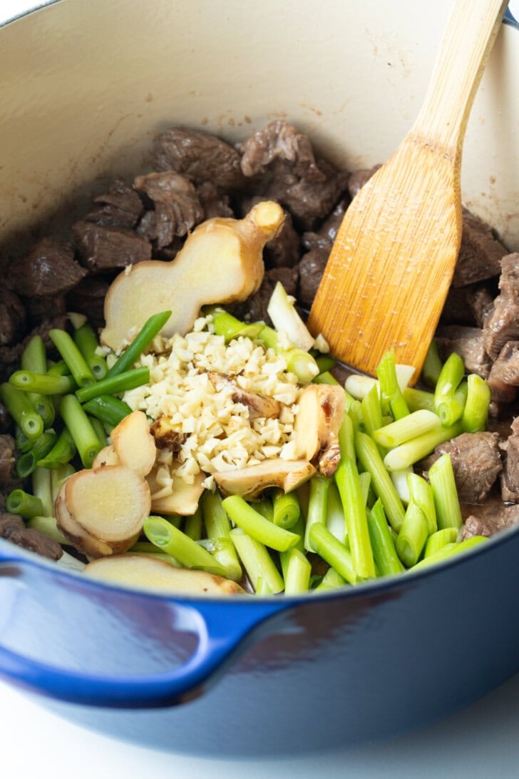 Cooking chunks of beef, ginger, beans, and garlic in a large pot with wooden spatula.