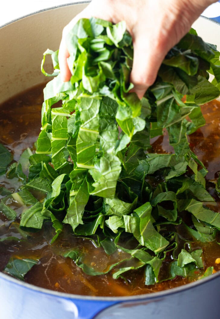 Hand adding chopped bok choy greens to the pot of broth.