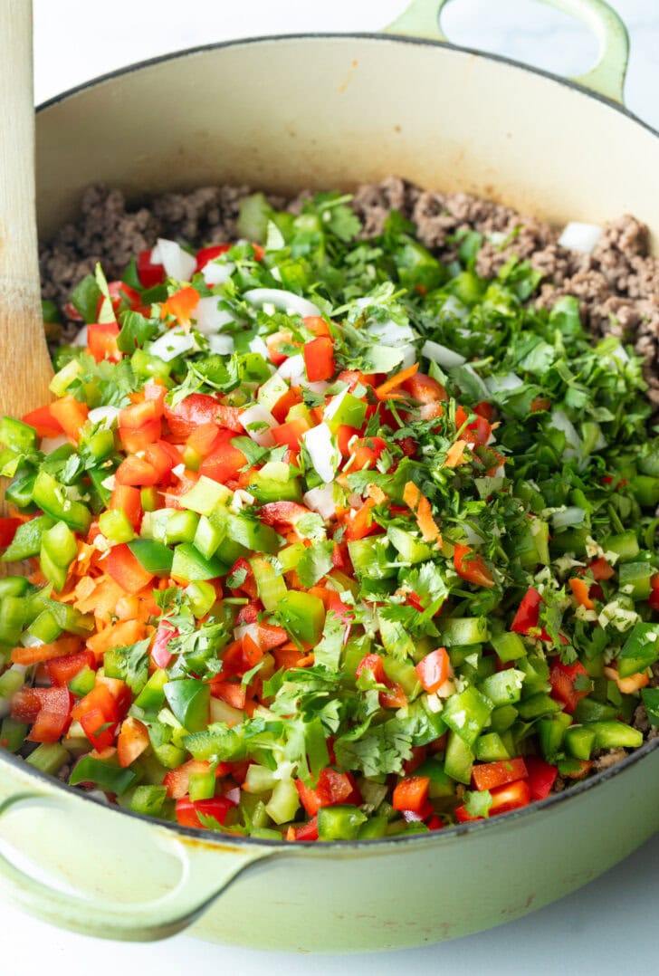 Adding chopped fresh peppers and herbs to pot of ground venision.