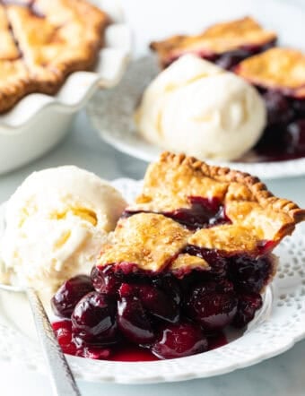 Slice of homemade cherry pie on a white plate, with scoop of vanilla ice cream on the side.