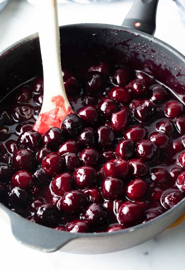 Cooking homemade cherry pie filling in a large pot, stirring with a wooden spoon.