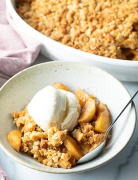 Top down view of a white bowl with golden apple crisp topped with a big scoop of ice cream.