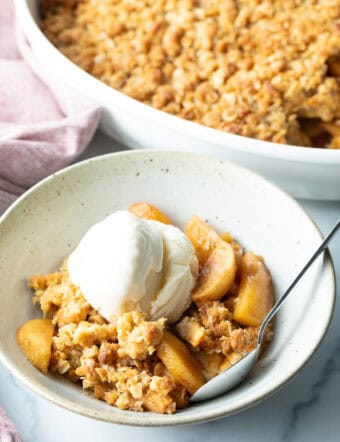 Top down view of a white bowl with golden apple crisp topped with a big scoop of ice cream.