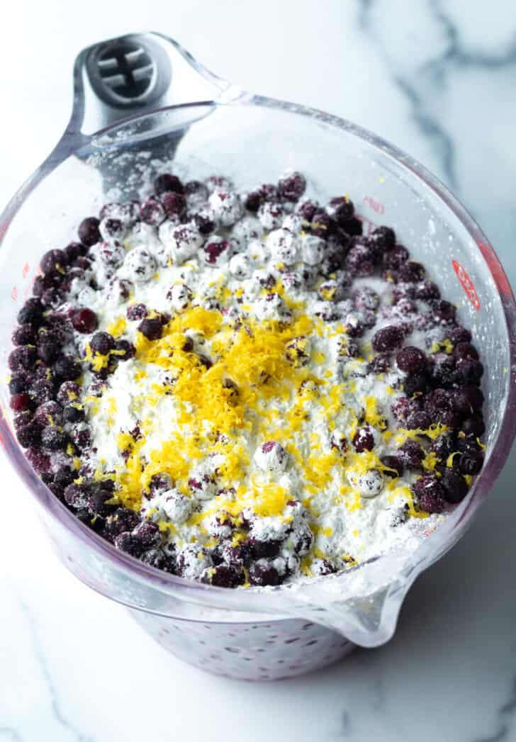 Combining blueberries, lemon zest, flour and sugar in a glass mixing bowl.