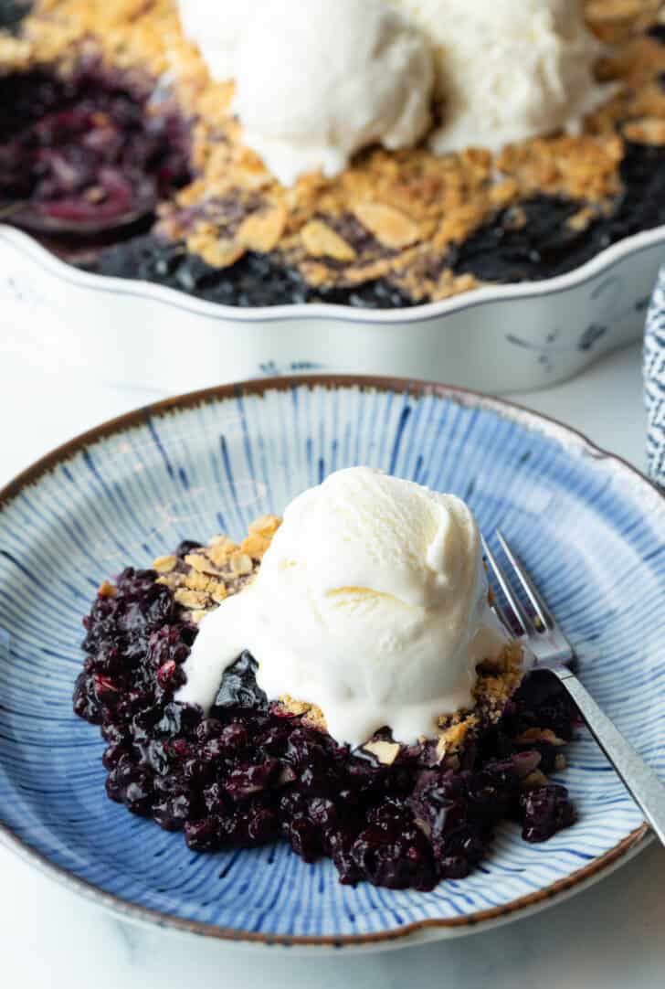 Serving of blueberry crumble on a plate, with scoop of ice cream on top.