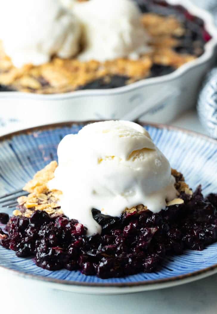 Serving of blueberry crumble on a plate, with scoop of ice cream on top.