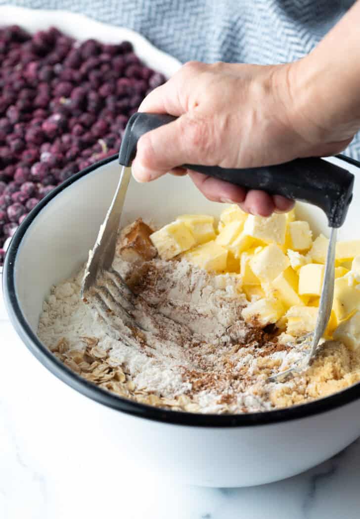 Hand with a pastry cutter, cutting butter into the topping mixture.