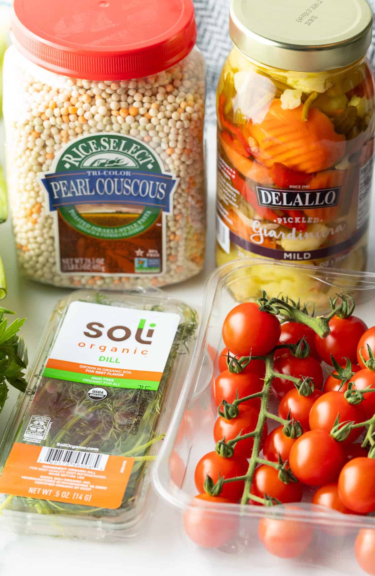 Recipe ingredients in individual containers: Pearl couscous, giardiniera pickled vegetables, on the vine cherry tomatoes, and fresh dill.