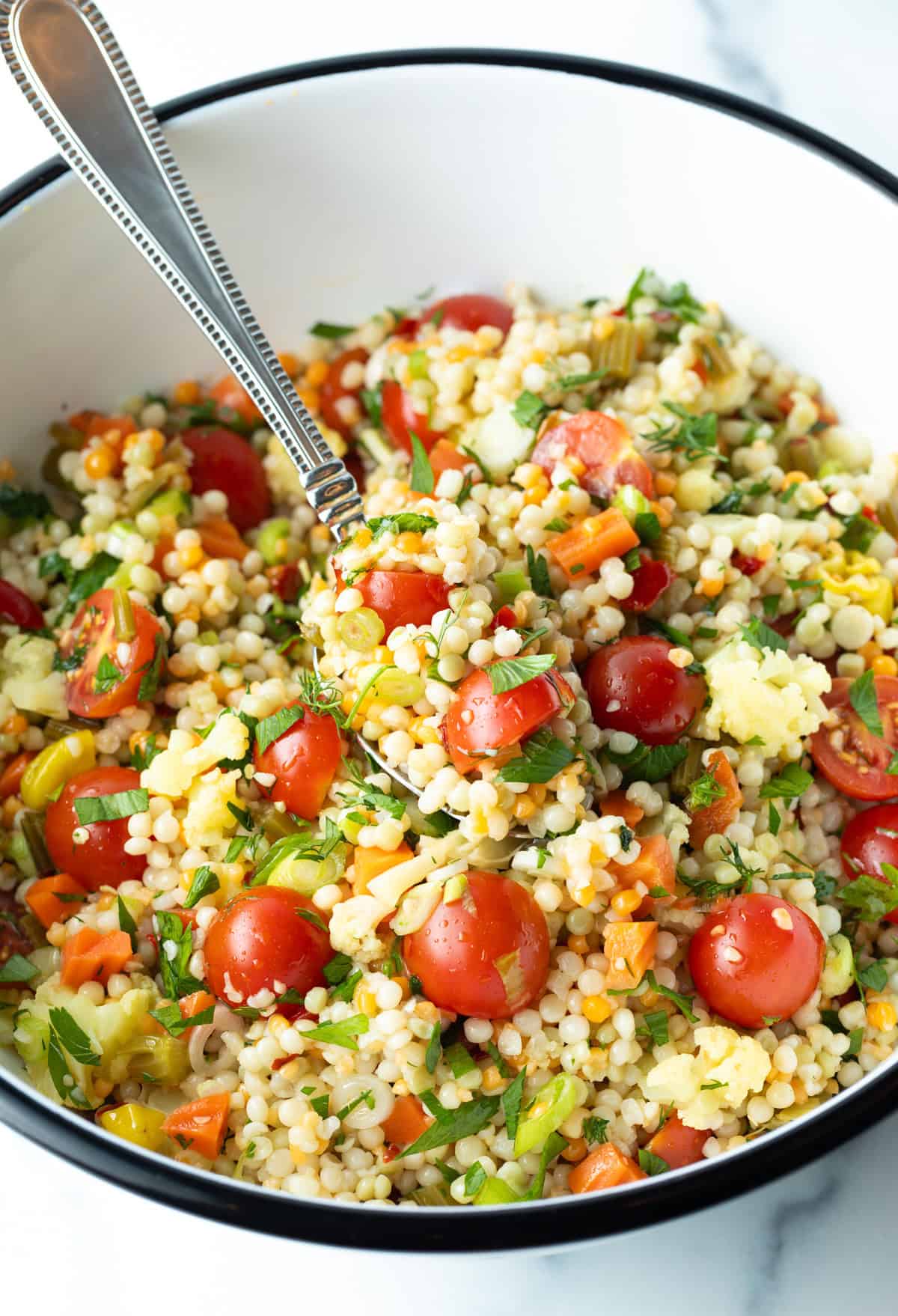 Pearl couscous salad with chopped tomatoes, fresh herbs, and pickled vegetables in a large white mixing bowl.