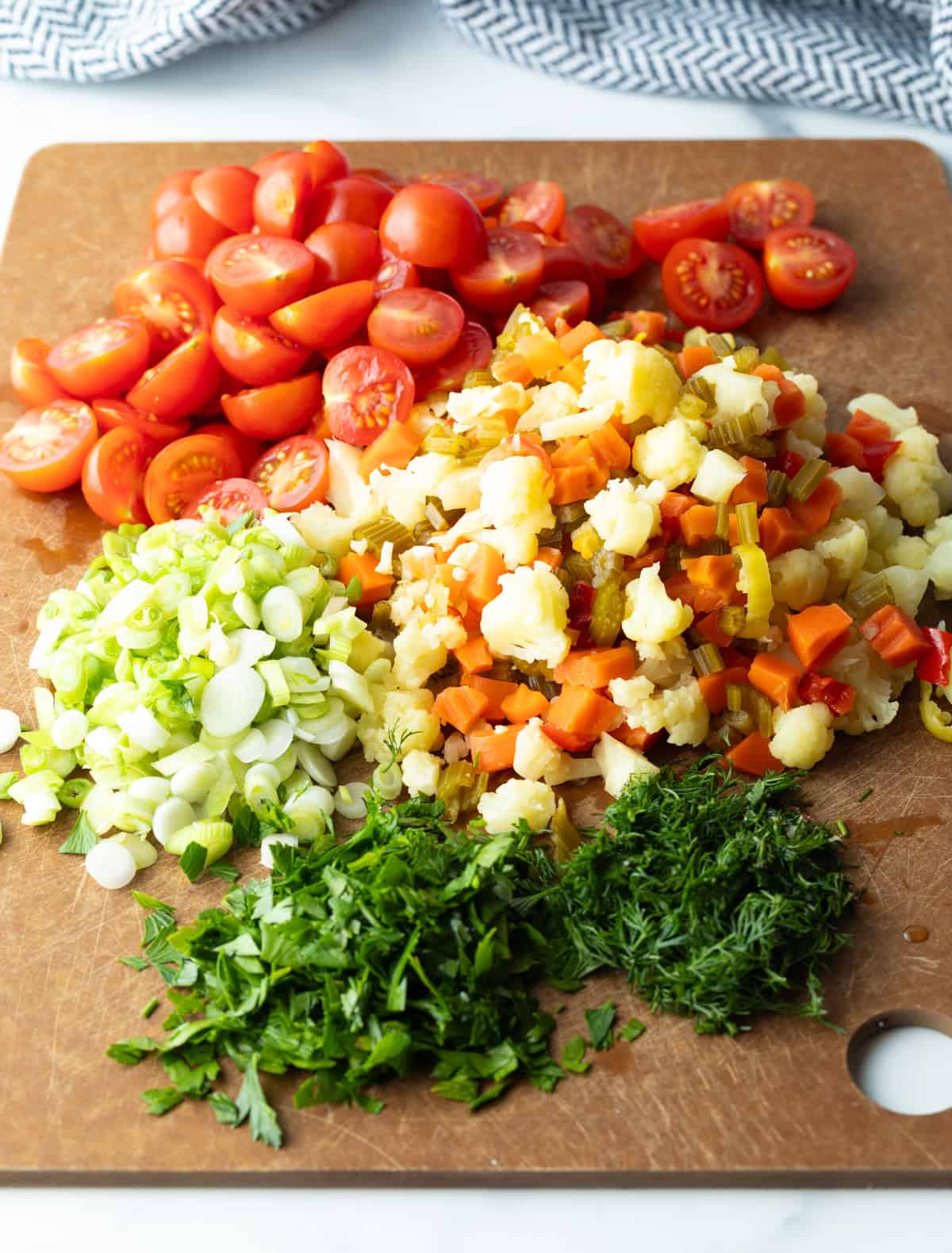 Chopped cherry tomatoes, scallions, parsley, and pickled vegetables in piles on a brown cutting board.