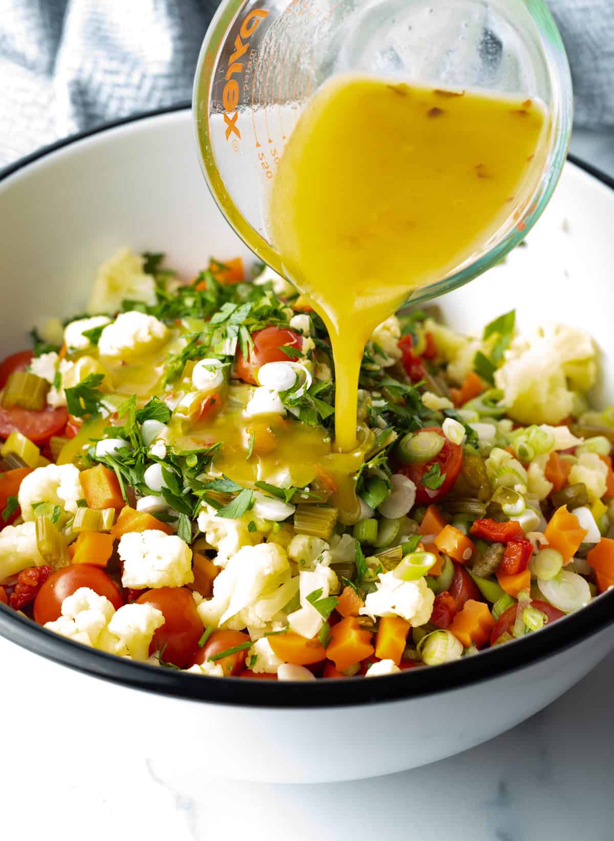 Pouring the dressing over the veggies in a large mixing bowl.