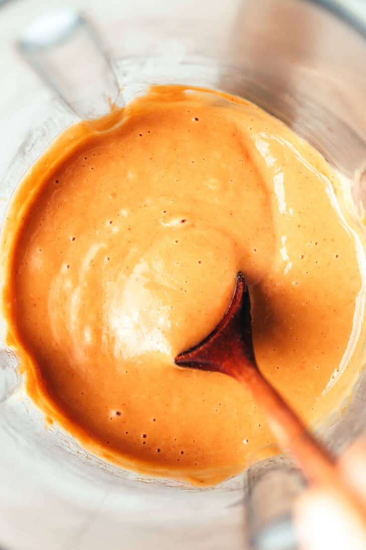 Wood spoon stirring peanut sauce in a blender jar.