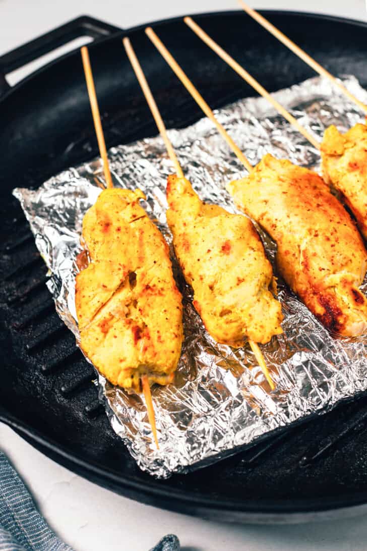 4 grilled chicken skewers resting on a baking sheet coated with foil.