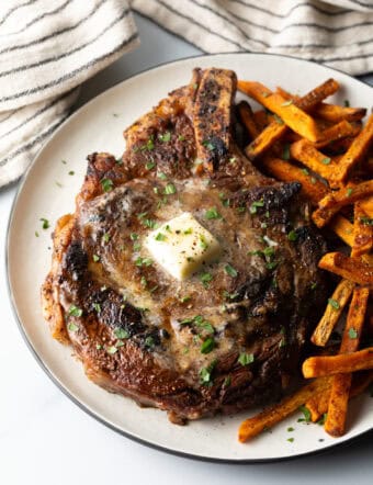 Large bone in ribeye steak on a plate with sweet potato fries.
