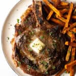 Large bone in ribeye steak on a plate with sweet potato fries.