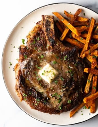 Large bone in ribeye steak on a plate with sweet potato fries.