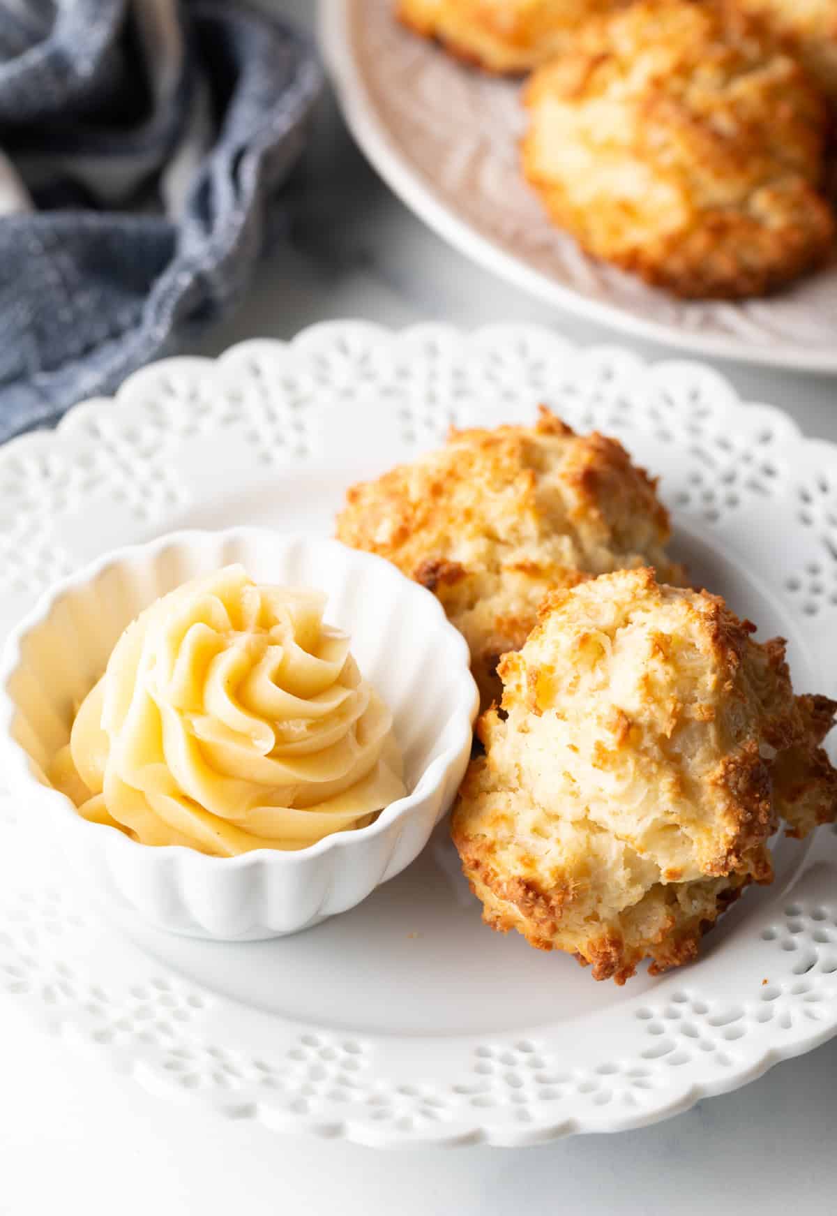 Two buttermilk drop biscuits on a white plate with a white ramekin of whipped honey butter.