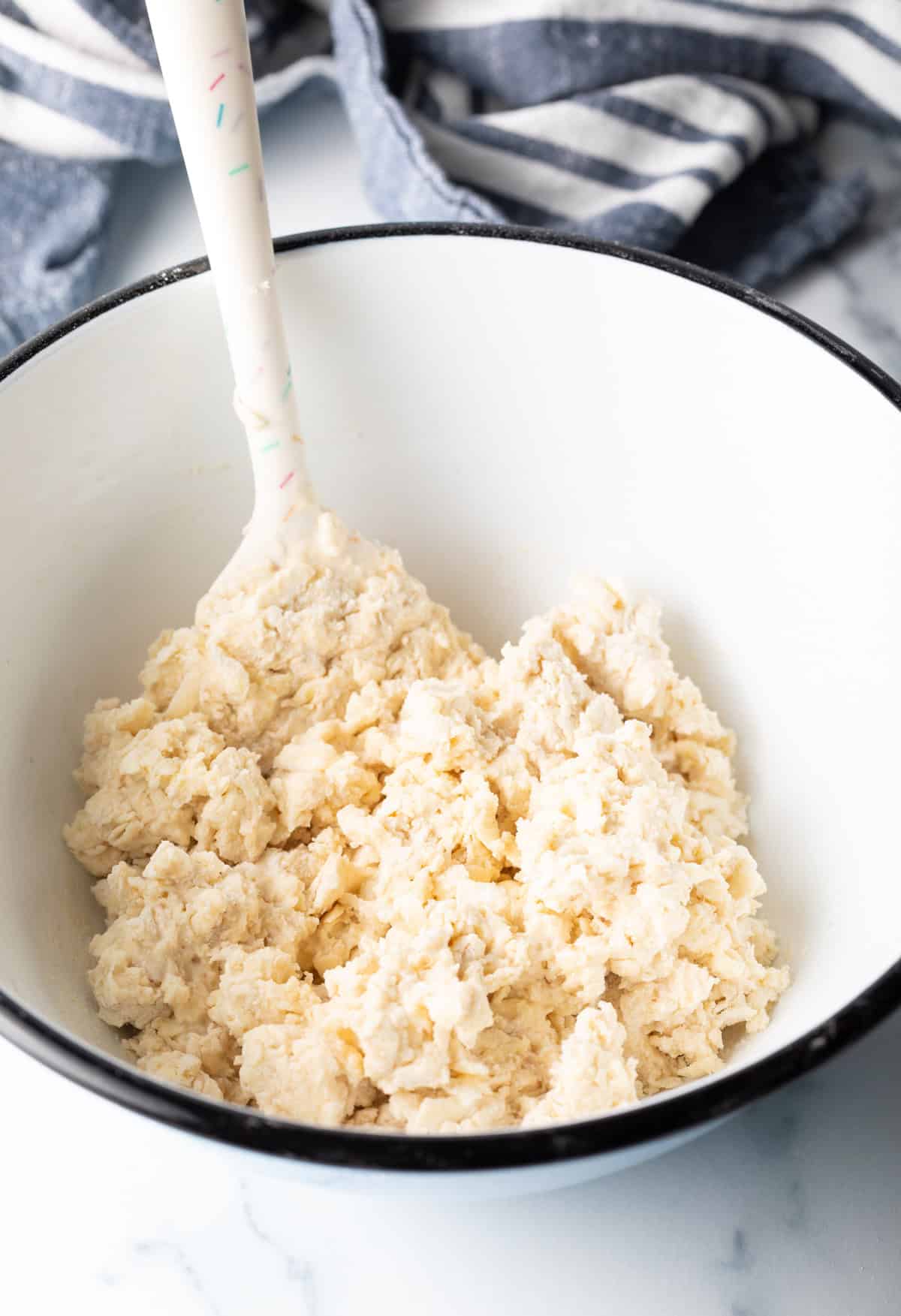 Sticky dough in a white bowl being stirred by a white spatula.