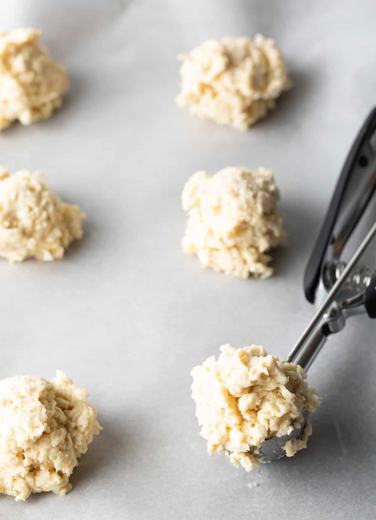 Using a metal cookie scoop to portion biscuit dough onto a baking sheet.