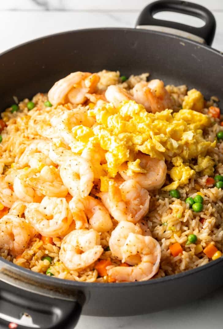 Deep black skillet with cooked shrimp, rice, scrambled eggs, and veggies.