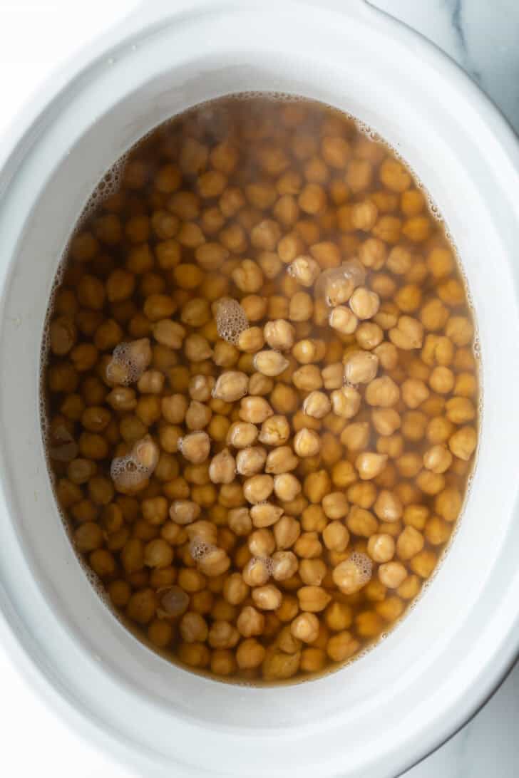 Top down white crockpot with chickpeas and water.