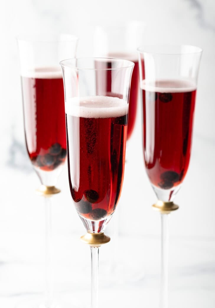 Four fluted glasses with deep red kir royale cocktail drinks.