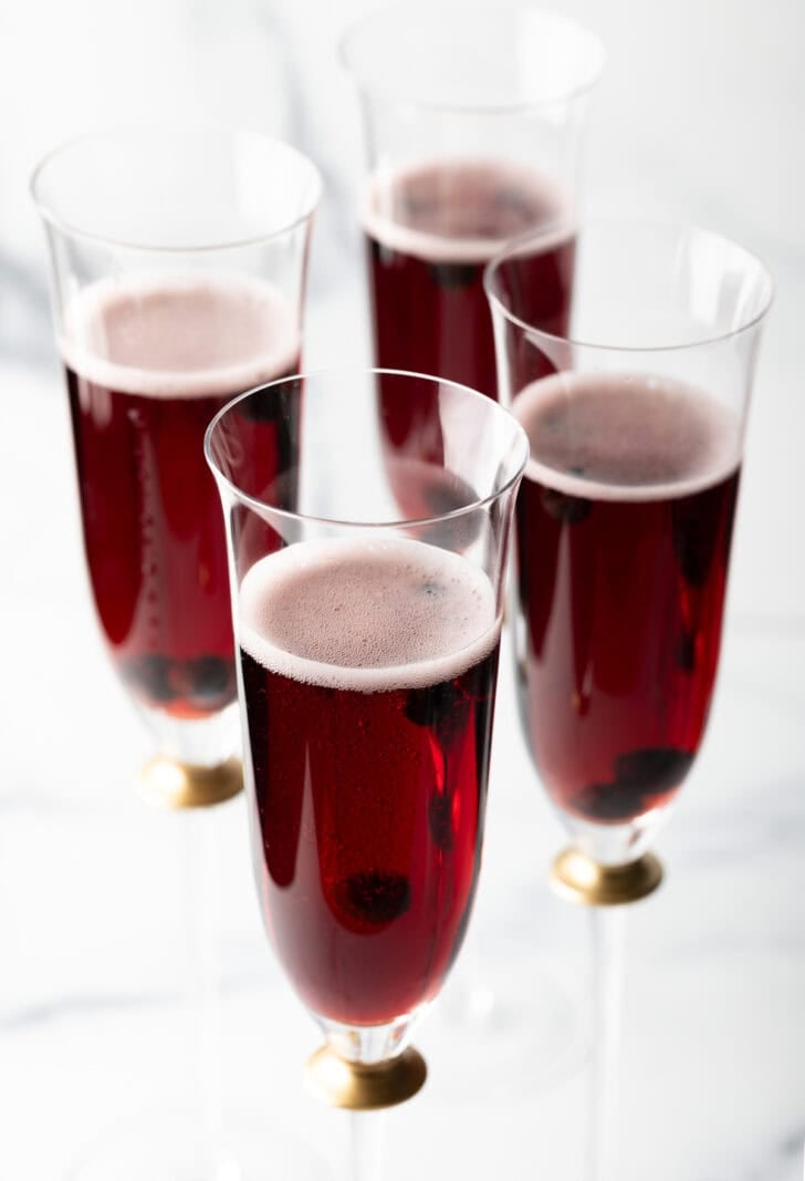 Four fluted glasses with deep red kir royale cocktail drinks.