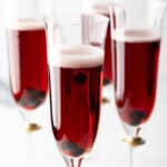 Four fluted glasses with deep red kir royale cocktail drinks.