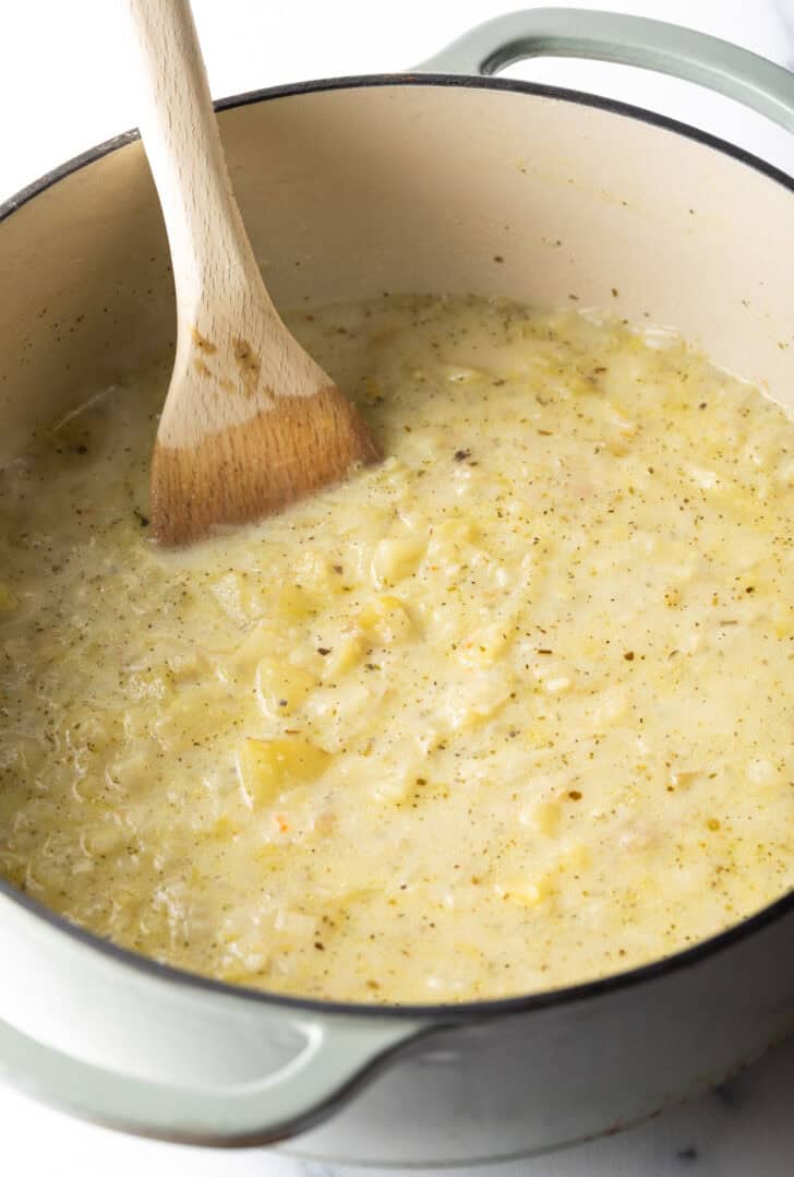 Wood spoon stirring a creamy batch of soup in a large pot.
