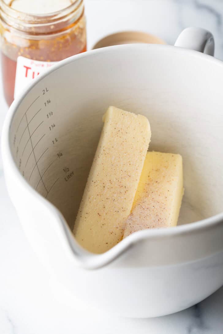 Two sticks of butter and spices in a large white mixing pitcher.