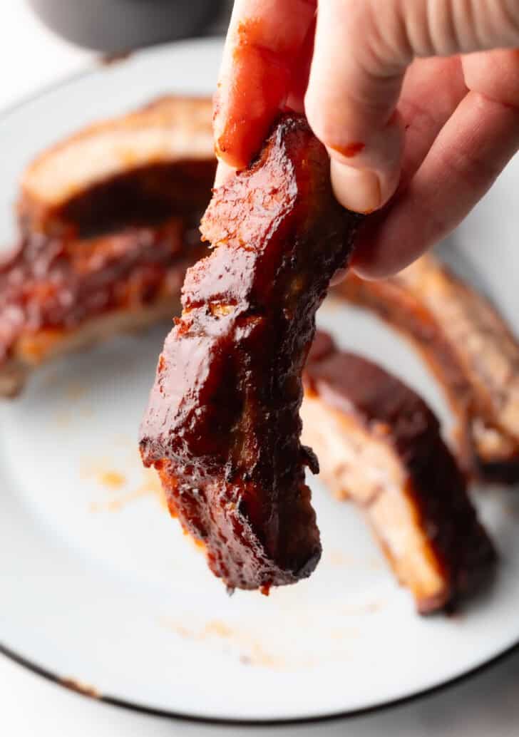 Hand holding a rib coated in barbecue sauce to camera.
