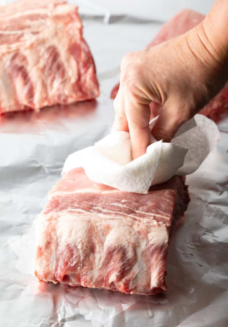 Hand using a paper towel to pat dry a small rack of baby back ribs.